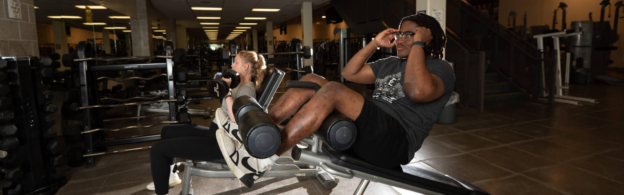 Two student staff working out in the Weight Room area of the Western student recreation centre on the equipment